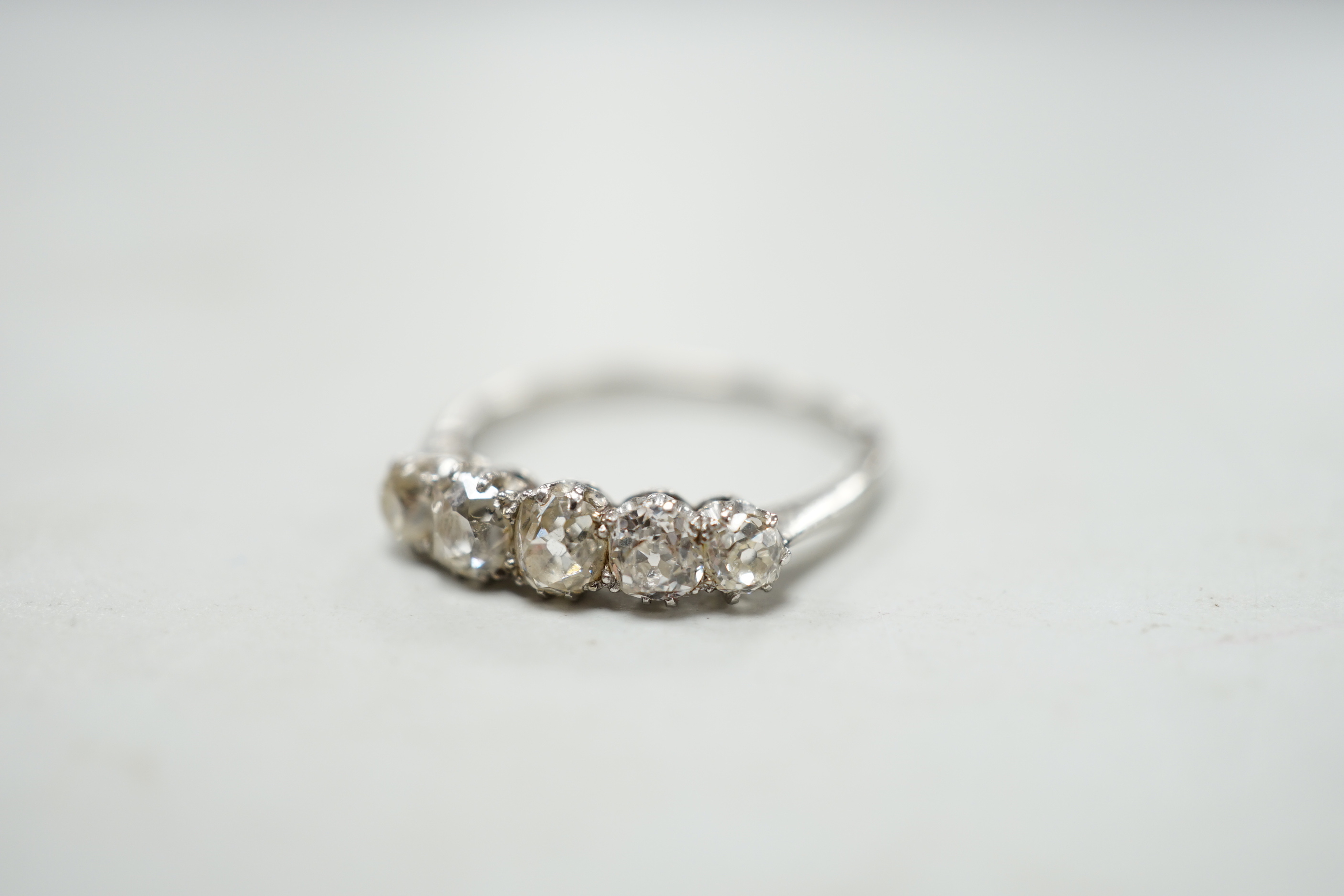 A 1940's white metal and graduated five stone diamond set half hoop ring, size M/N, gross weight 2.8 grams.